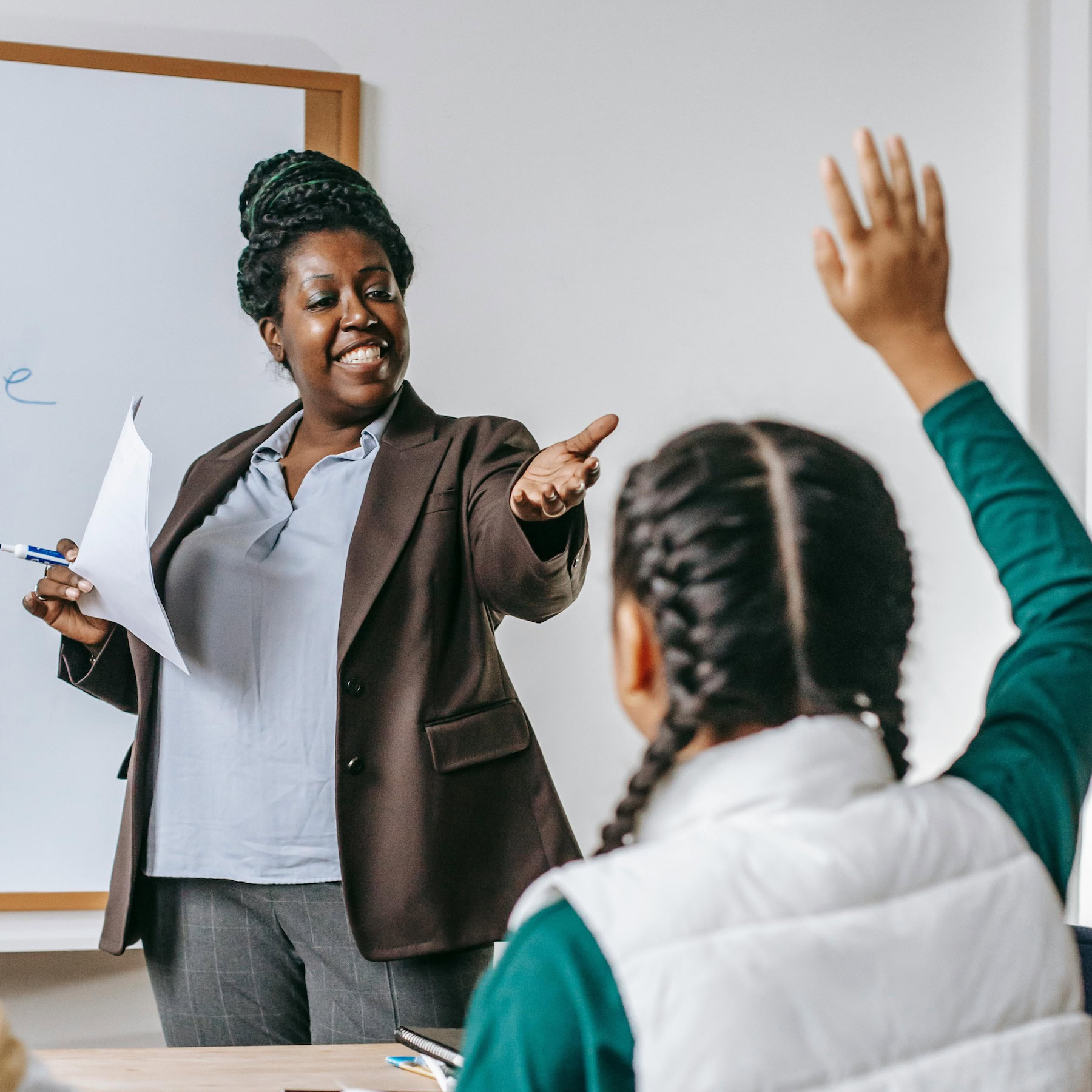 A teacher points to a student with their hand raised.